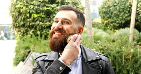 Photo for Young bearded man brushing his beard outdoor. - Royalty Free Image