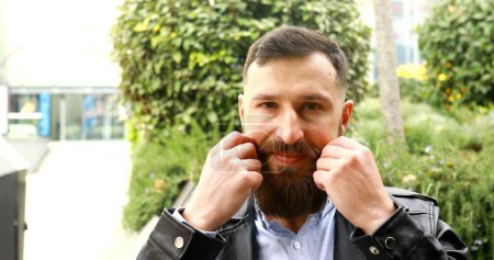 Téléchargez les photos : Homme barbu frisant sa moustache en plein air et le déplaçant drôle. - en image libre de droit
