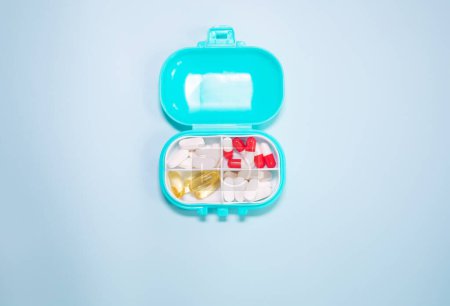 Téléchargez les photos : Boîte en plastique avec différentes pilules sur fond bleu clair - en image libre de droit