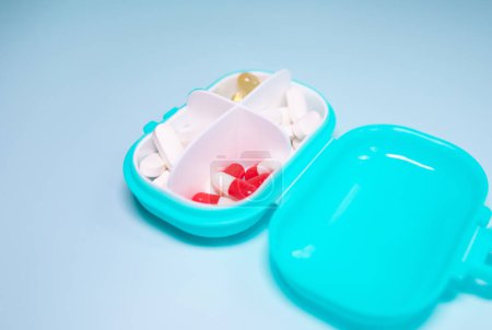 Foto de Caja de plástico con diferentes píldoras sobre fondo azul claro - Imagen libre de derechos