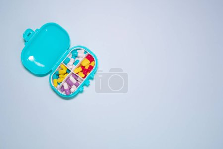Téléchargez les photos : Boîte en plastique avec différentes pilules sur fond bleu clair. Espace pour le texte - en image libre de droit