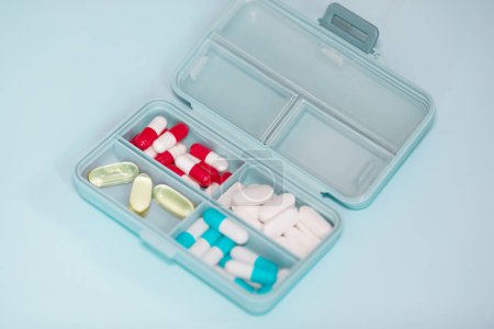 Téléchargez les photos : Boîte en plastique avec différentes pilules sur fond bleu clair. Espace pour le texte - en image libre de droit