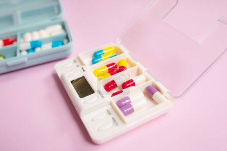 Téléchargez les photos : Boîtes en plastique avec différentes pilules sur fond rose clair - en image libre de droit