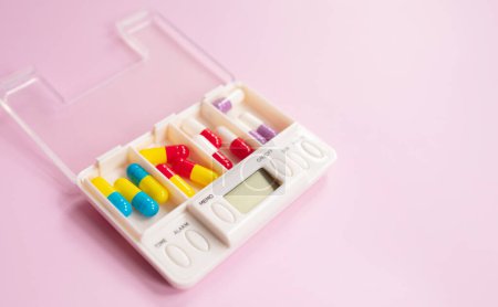 Téléchargez les photos : Boîte en plastique avec différentes pilules sur fond rose clair. Espace pour le texte - en image libre de droit