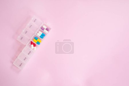 Téléchargez les photos : Boîte en plastique avec différentes pilules sur fond rose clair. Espace pour le texte - en image libre de droit