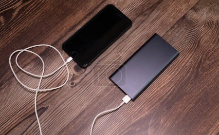 Photo for Powerbank charging smartphone on wooden background. - Royalty Free Image