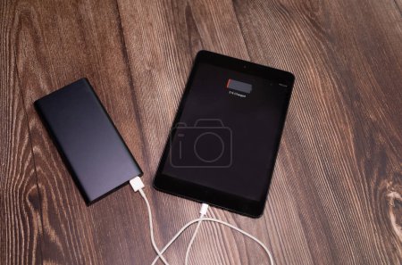 Photo for Tablet charging with energy bank on wooden table. - Royalty Free Image