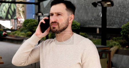 Photo for Serious young man talking on mobile phone in the street - Royalty Free Image