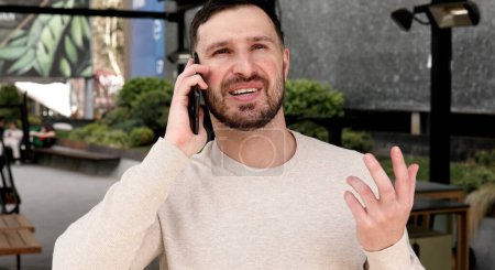 Téléchargez les photos : Jeune homme émotionnel parlant au téléphone dans la rue - en image libre de droit