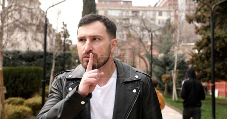 Photo for Shh, be quiet. Portrait of bearded man making silence gesture with finger on his lips, keeping some secret, while posing at the street - Royalty Free Image
