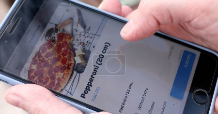 Foto de Tbilisi, Georgia - 28 de marzo de 2023: Hombre que ordena pizza usando la entrega en línea. Man Ordering Food In Online Store Using a Smartphone (en inglés). Hombre Pedir pizza utilizando la aplicación de entrega de alimentos. - Imagen libre de derechos