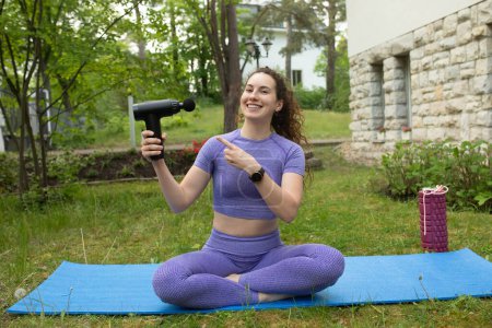 Photo for Young fit woman pointing at percussion massager and smiling at camera outdoor - Royalty Free Image