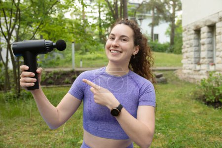 Photo for Beautiful smiling young fit woman holding percussion massager outdoor - Royalty Free Image