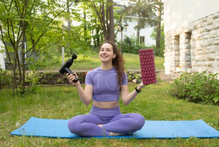 Photo for Young fit woman holding yoga roller and percussion massager outdoor - Royalty Free Image