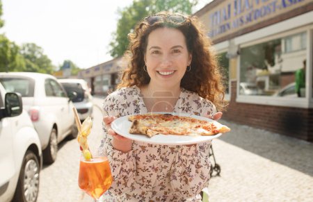 Téléchargez les photos : Femme mangeant une délicieuse pizza en plein air dans un café de rue. Restauration rapide à emporter dans une journée ensoleillée
. - en image libre de droit