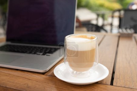 Téléchargez les photos : Coupe de café et ordinateur portable sur une table en bois dans un espace de co-travail de café. Affaires en ligne, travail de café, concept de bureau portable, gros plan - en image libre de droit