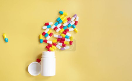 Photo for Pile of colorful pills and container on yellow background. - Royalty Free Image