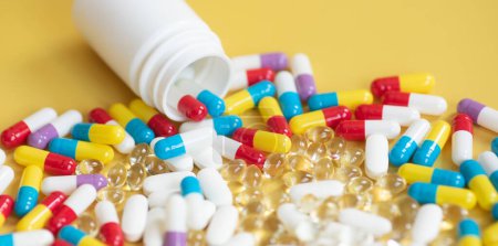 Téléchargez les photos : Vue rapprochée des pilules et capsules colorées avec récipient sur fond jaune - en image libre de droit