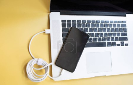 Téléchargez les photos : Ordinateur portable et téléphone intelligent avec câble d'alimentation pour charger sur fond jaune. - en image libre de droit