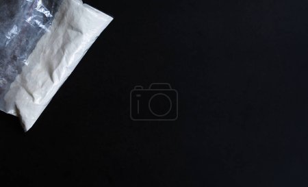 Téléchargez les photos : Sac en plastique blanc de drogues, sac avec poudre blanche sur fond noir - en image libre de droit