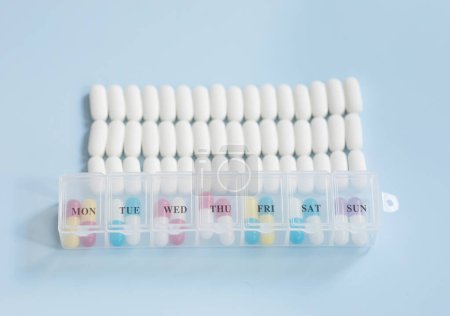 Téléchargez les photos : Beaucoup de pilules médicinales et boîte à pilules sur fond bleu. Pilules blanches dispersées sur la table bleue. - en image libre de droit