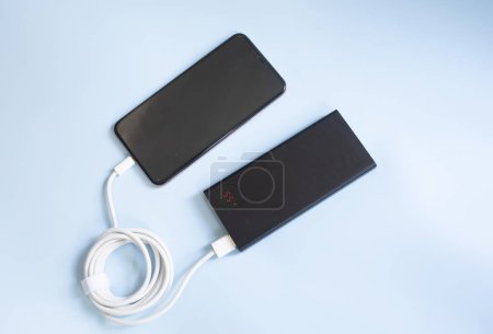 Foto de Un smartphone cargando con powerbank negro sobre fondo azul. Vista de primer plano con espacio de copia. - Imagen libre de derechos