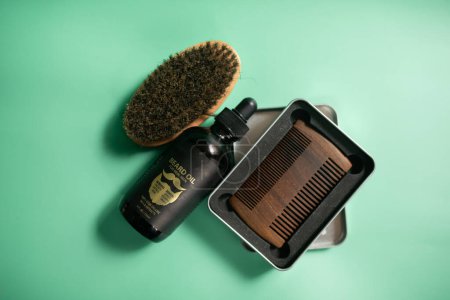 Téléchargez les photos : Outils de salon de coiffure sur fond vert. Peigne de barbe en bois vintage, huiles de barbe, ciseaux, tondeuse électrique, brosse et baume. - en image libre de droit