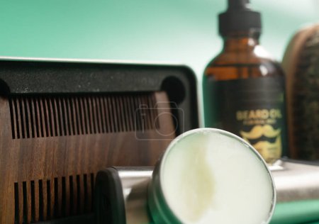 Téléchargez les photos : Outils de salon de coiffure sur fond vert. Peigne de barbe en bois vintage, huiles de barbe, ciseaux, tondeuse électrique, brosse et baume. - en image libre de droit