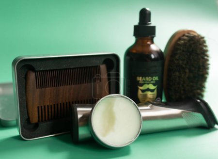 Photo for Barber shop tools on green background. Vintage wooden beard comb, beard oils, scissors, electric trimmer, brush and balm. - Royalty Free Image