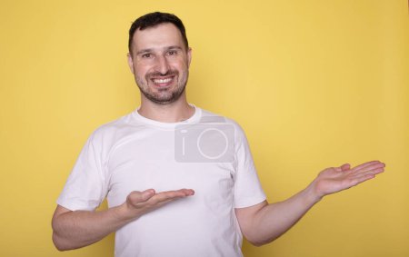 Foto de Joven guapo en camiseta blanca presentando algo sobre fondo amarillo - Imagen libre de derechos
