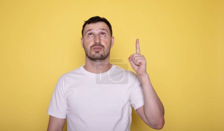Téléchargez les photos : Homme pointant vers le haut avec le doigt à l'espace de copie sur fond jaune. - en image libre de droit