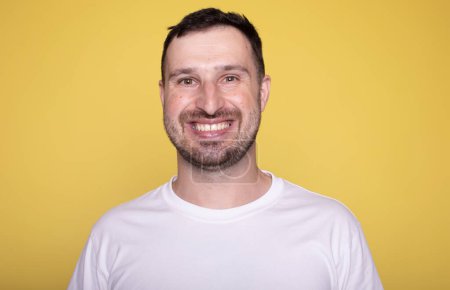 Téléchargez les photos : Portrait d'homme heureux en t-shirt blanc sur fond jaune studio - en image libre de droit