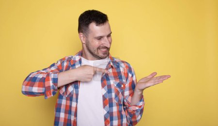 Photo for Portrait of a handsome man pointing at something on a yellow background - Royalty Free Image