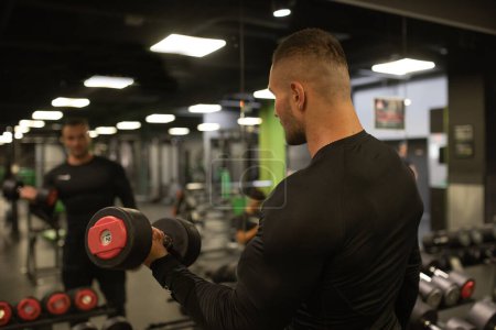 Téléchargez les photos : S'adapter jeune homme en tenue de sport soulever du poids lors d'un cours d'exercice dans une salle de gym. - en image libre de droit