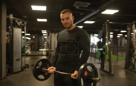 Foto de Hombre musculoso haciendo ejercicio en el gimnasio haciendo ejercicios con barra en el bíceps
. - Imagen libre de derechos