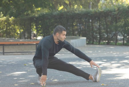 Foto de Guapo joven deportista haciendo ejercicios de estiramiento al aire libre - Imagen libre de derechos