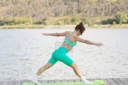 Téléchargez les photos : Concept de forme physique et de style de vie. Jeune femme sportive étirant les muscles dans un parc en face du lac. Femme athlétique étirement. - en image libre de droit