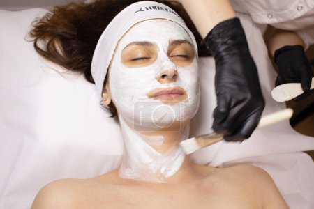 Foto de Joven hermosa mujer recibiendo máscara facial blanca en el salón de belleza del spa. - Imagen libre de derechos