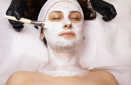 Téléchargez les photos : Jeune belle femme recevant un masque facial blanc dans un salon de beauté spa. - en image libre de droit