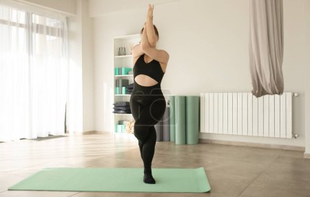 Téléchargez les photos : Jeune femme séduisante sportive pratiquant le yoga, faisant l'exercice des bras Garudasana, pose d'aigle dans le studio de yoga. - en image libre de droit