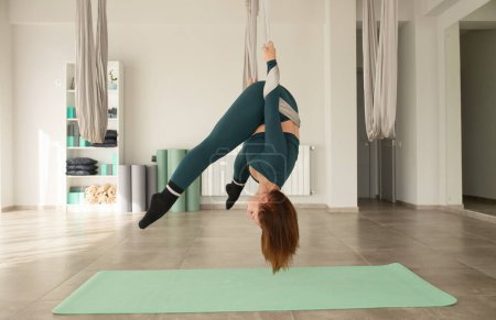 Téléchargez les photos : Jeune femme pratiquant le yoga de mouche dans la salle de gym. Entraîneur de yoga aéro tenant des sangles dans les mains. - en image libre de droit