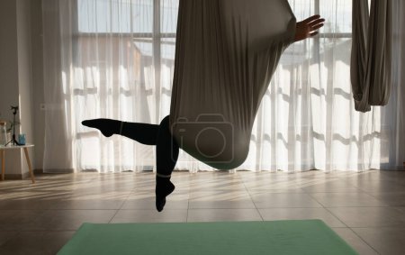 Foto de Mujer joven practicando yoga con mosca en el gimnasio. Chica entrenadora de aero yoga sujetando correas en las manos. - Imagen libre de derechos