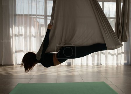 Foto de Mujer joven practicando yoga con mosca en el gimnasio. Chica entrenadora de aero yoga sujetando correas en las manos. - Imagen libre de derechos
