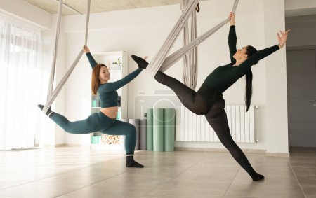 Foto de Dos mujeres haciendo ejercicio con correas durante el yoga con mosca. Clase de Aero yoga. - Imagen libre de derechos