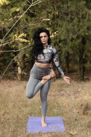 Téléchargez les photos : Jolie femme faisant des exercices de yoga dans le parc d'automne. Belle femme pratiquant le yoga seule dans la forêt. - en image libre de droit