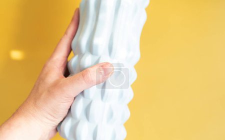 Photo for Close-up of person holding blue massage foam roller on yellow background. - Royalty Free Image