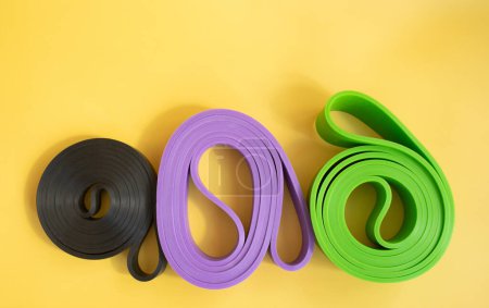 Téléchargez les photos : Ensemble de bandes de caoutchouc colorées pour la forme physique sur fond jaune. concept sportif. - en image libre de droit
