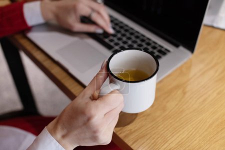 Foto de Primer plano de las manos de la mujer de negocios con el ordenador portátil que sostiene la taza de café en la oficina - Imagen libre de derechos