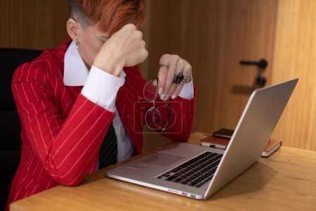 Foto de Mujer de negocios de mediana edad estresada en traje rojo que sufre de dolor de cabeza después del trabajo de computadora en la oficina. - Imagen libre de derechos