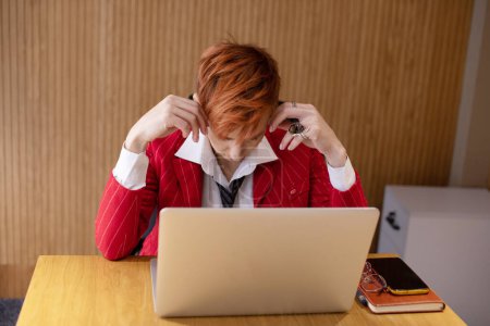 Foto de Mujer de negocios de mediana edad estresada en traje rojo que sufre de dolor de cabeza después del trabajo de computadora en la oficina. - Imagen libre de derechos